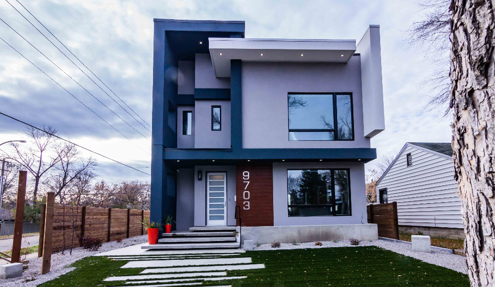 centered in frame modern geometric home with grey trim and blue, while and brown rectangles. a small yard is visible with red planters and overcast sky.